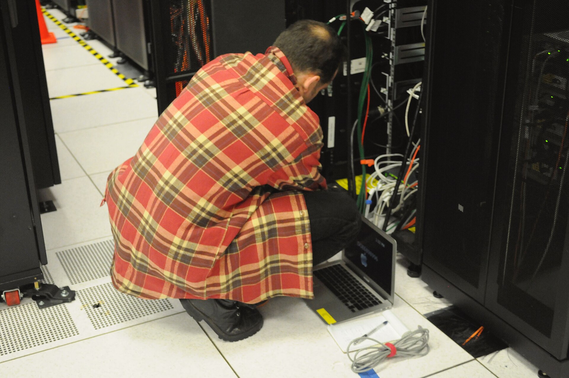 Technician checks a laptop beside server racks during infrastructure work